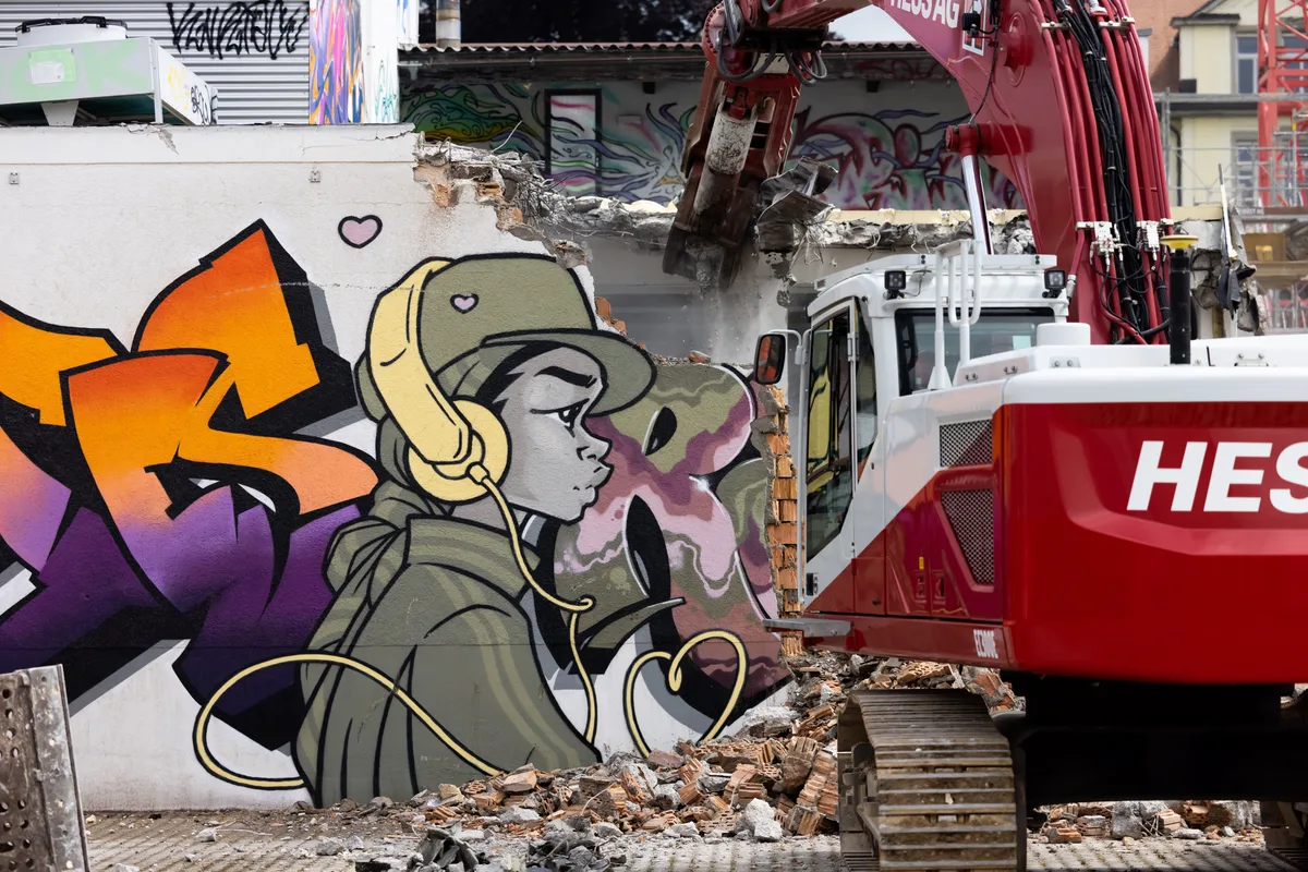 Man sieht noch den Rest eines Graffitis an einer Wand, die gerade abgebrochen wird.